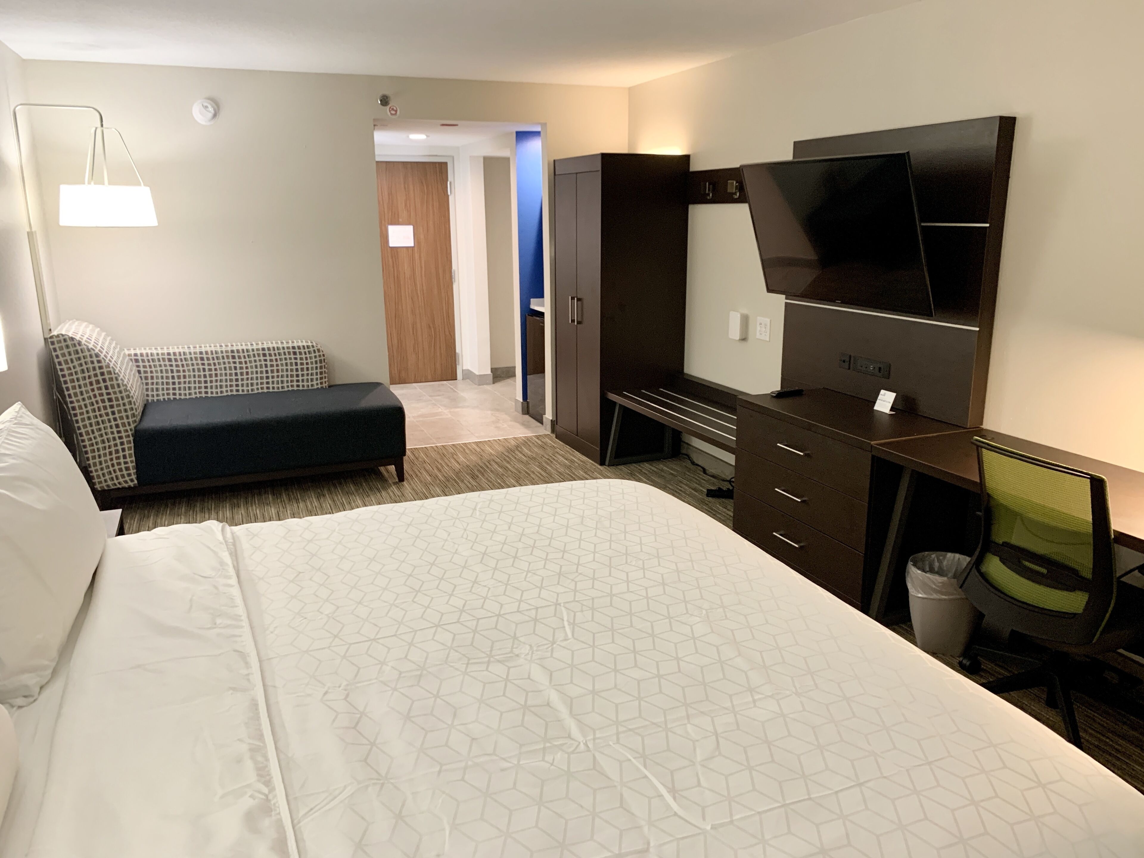 Una habitación de hotel con una cama grande, un escritorio con una silla, televisión y sofá.