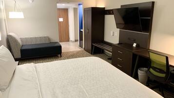 Una habitación de hotel con una cama grande, un escritorio con una silla, televisión y sofá.