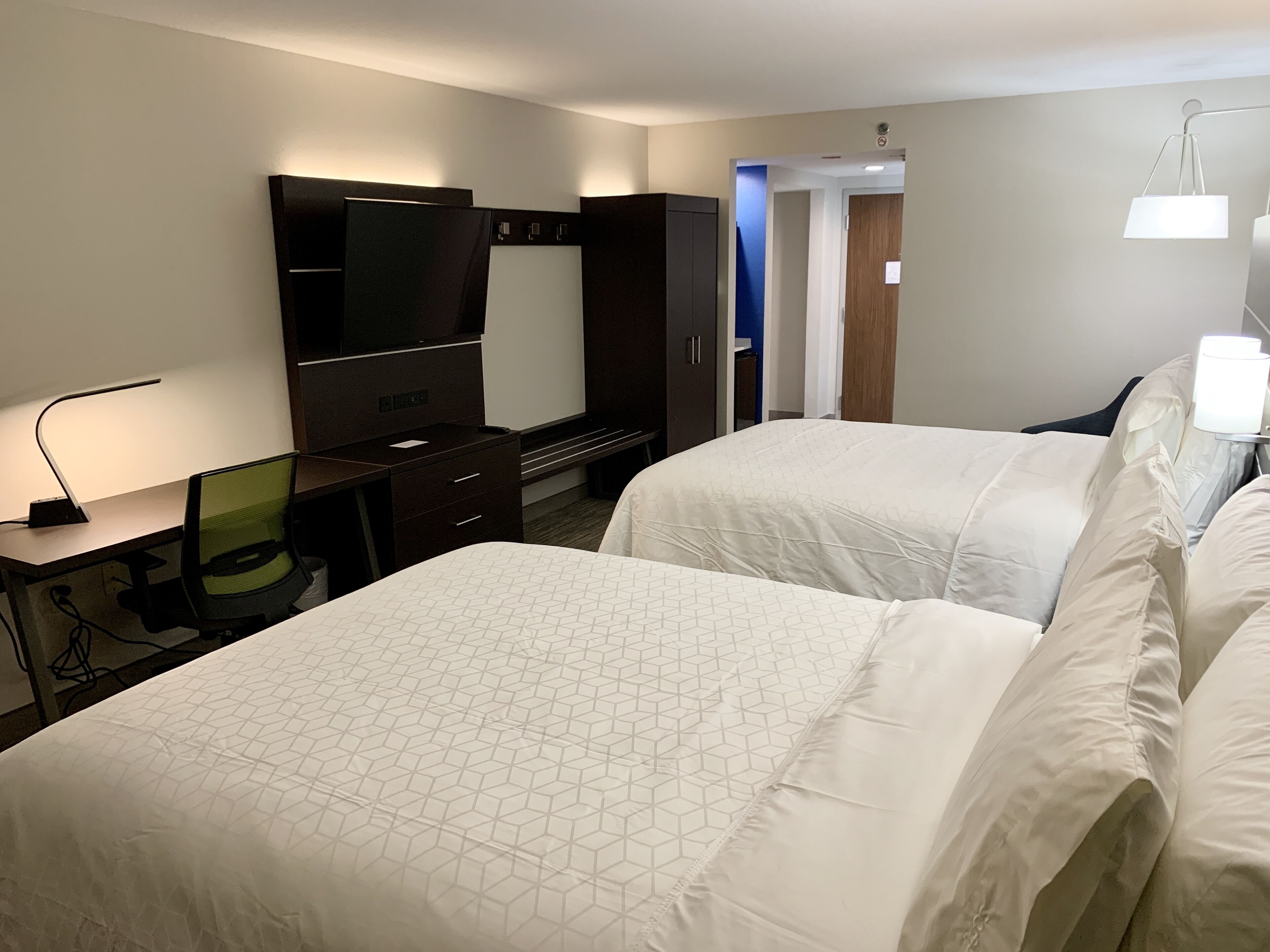 A hotel room with two beds, a desk with a computer, a TV, and a wardrobe.