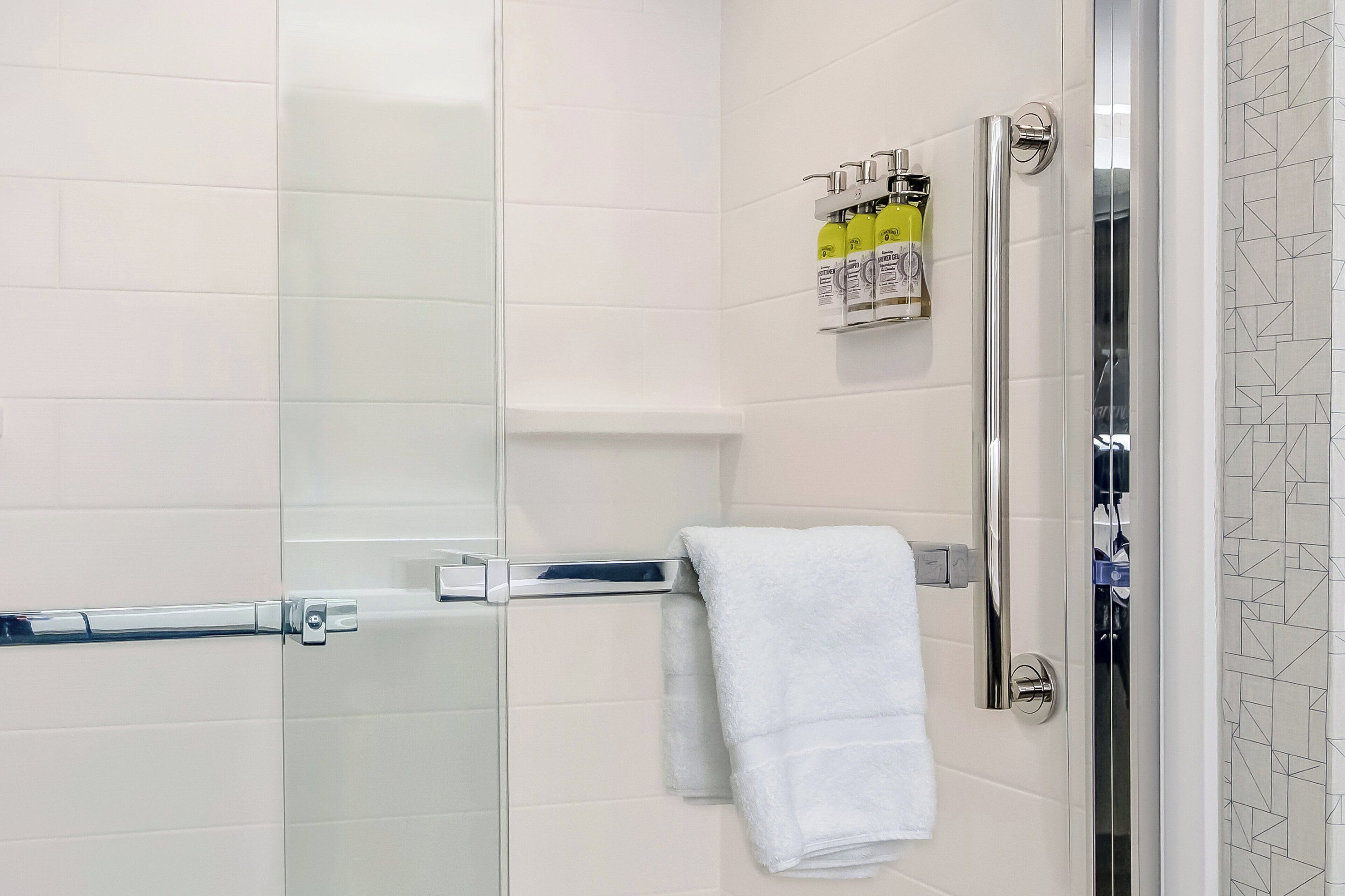 A modern bathroom with a glass shower enclosure, a white towel, and toiletries on a shelf.