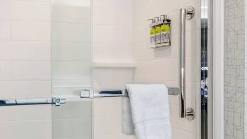A modern bathroom with a glass shower enclosure, a white towel, and toiletries on a shelf.