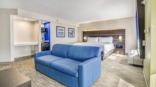 A hotel room with a blue sofa, a bed with white bedding, a microwave, and a small kitchenette. - Holiday Inn Express & Suites Longview North by IHG (Longview)