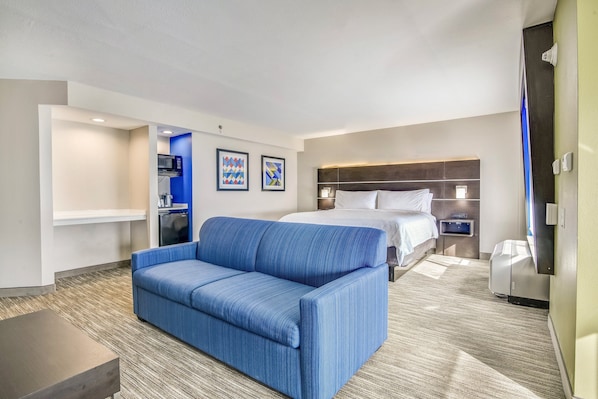 Une chambre d’hôtel avec un canapé bleu, un lit avec une literie blanche, un four à micro-ondes et une petite kitchenette.