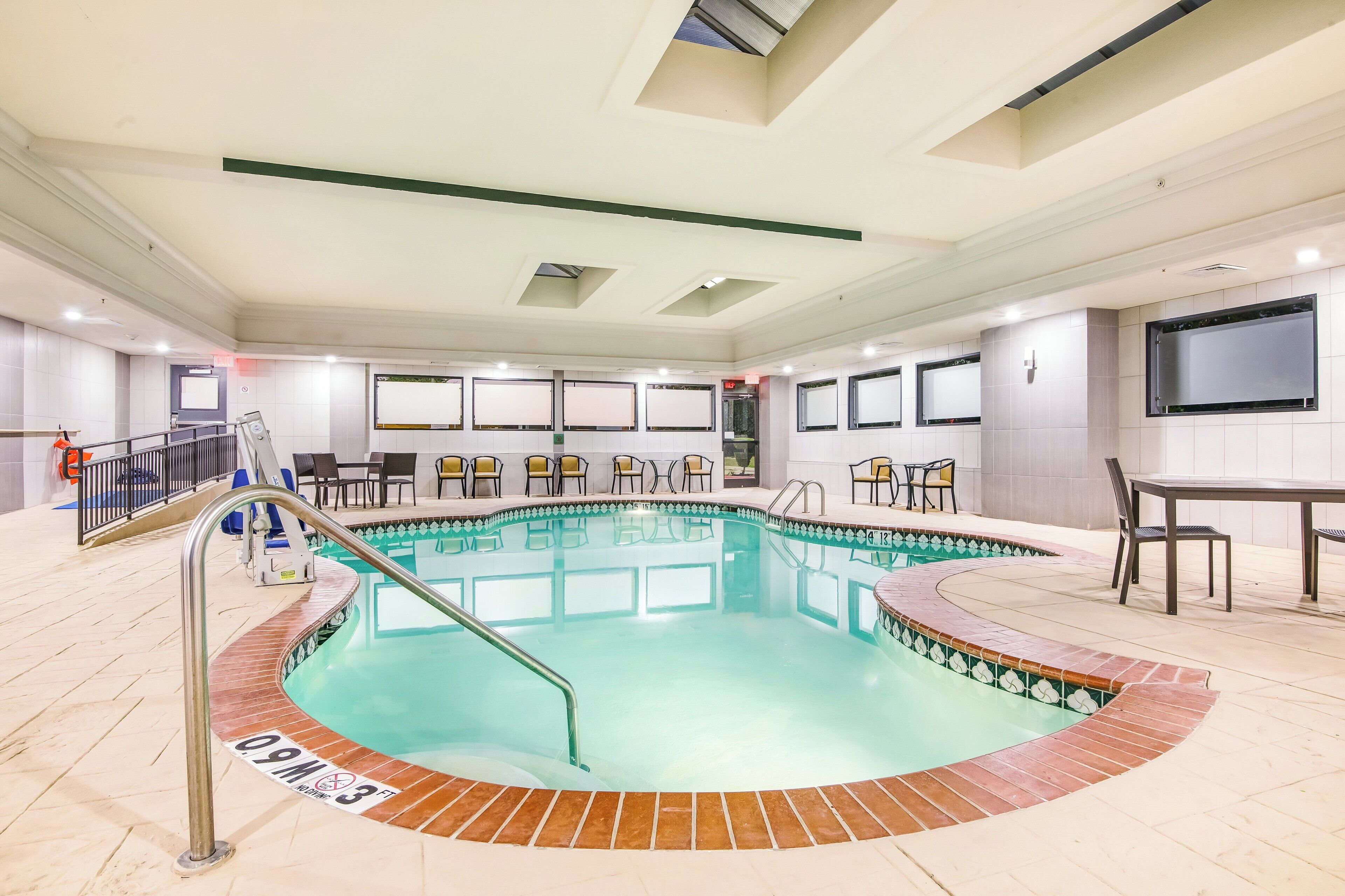 A swimming pool with a tiled deck, a changing room, and a seating area with chairs.