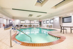 Una piscina con borde de baldosas, un vestuario y una zona de estar con sillas.