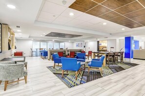 Un moderno vestíbulo de hotel con una variedad de zonas de estar, incluyendo sofás y sillones, un mostrador de recepción y una alfombra estampada.