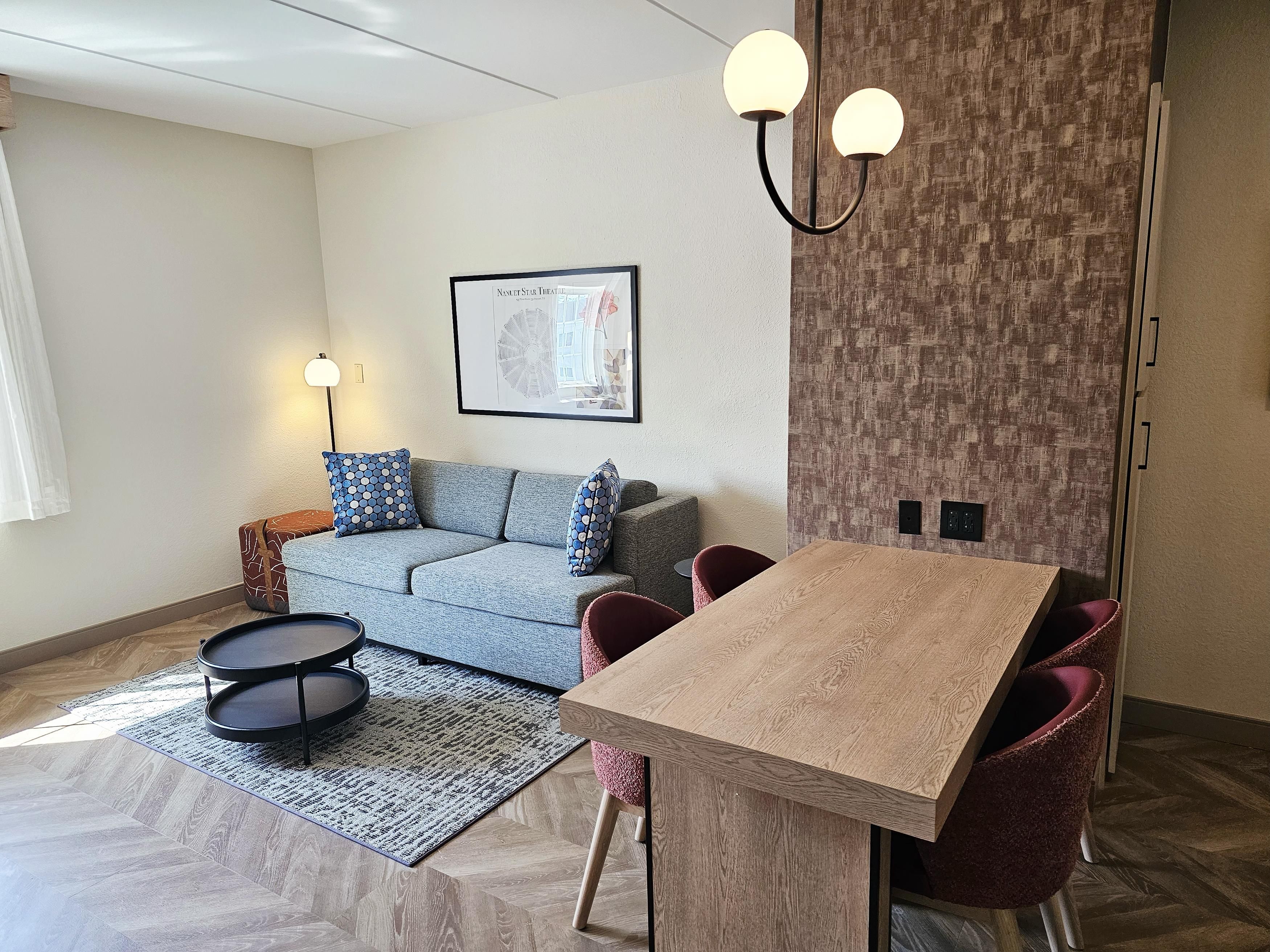 Una sala de estar moderna con un sofá, una mesa de comedor con sillas, un tapete estampado y un aplique de pared.