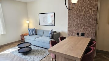 Una sala de estar moderna con un sofá, una mesa de comedor con sillas, un tapete estampado y un aplique de pared.