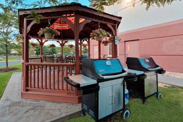 A gazebo with hanging flower baskets, two barbecue grills, and a patio area.