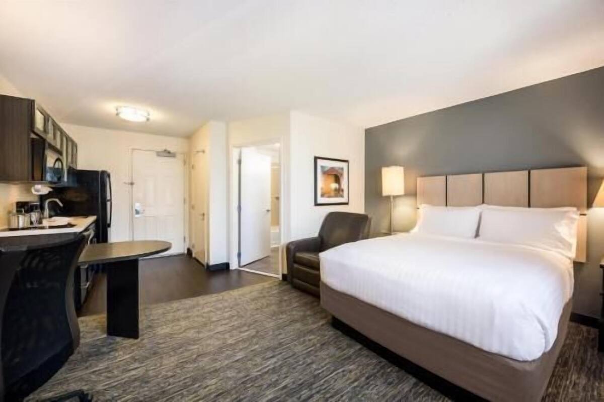 Een hotelkamer met een bed, een bureau, een stoel en een kitchenette.