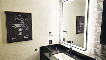 Un bagno con un lavandino nero, uno specchio grande con una luce e un disegno di brevetto incorniciato appeso al muro.