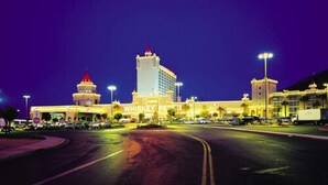 A hotel with a prominent casino sign, a large tower, and a well-lit parking area at night.