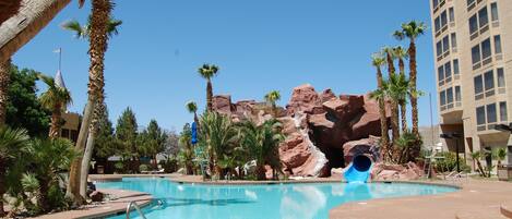 Une piscine avec un toboggan, des palmiers et une formation rocheuse.