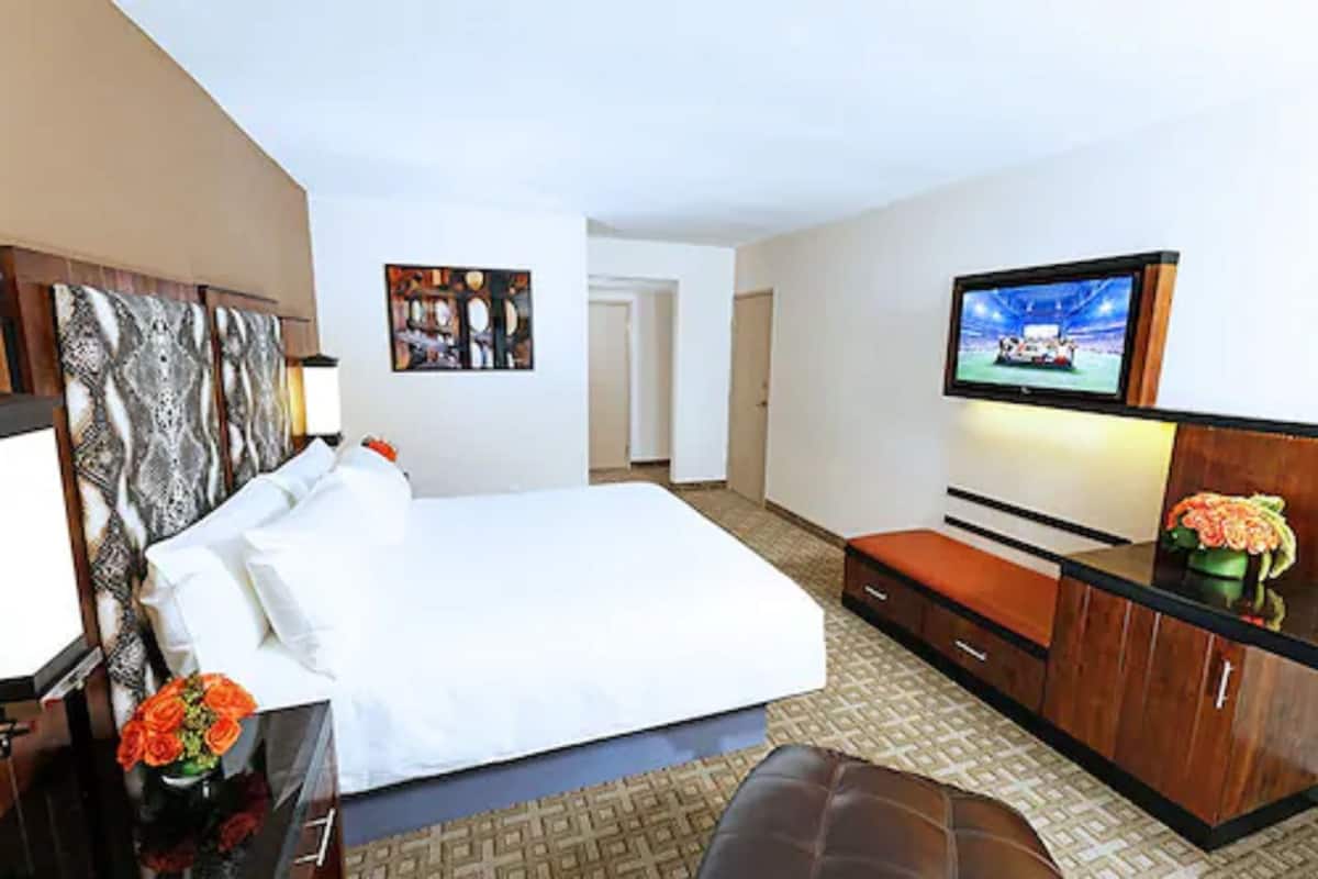Ett hotellrum med en stor säng, en tv som är monterad på väggen, ett skrivbord med en stol och en liten sittgrupp.