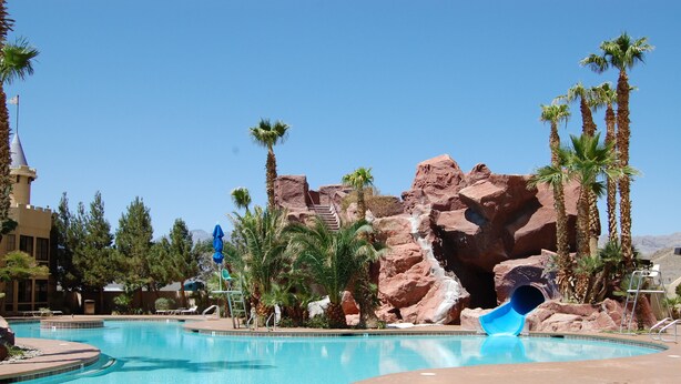 A swimming pool with a blue slide, palm trees, and rocky formations.