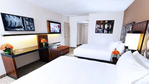 A hotel room with two beds, a desk, a chair, a TV, and artwork on the walls.