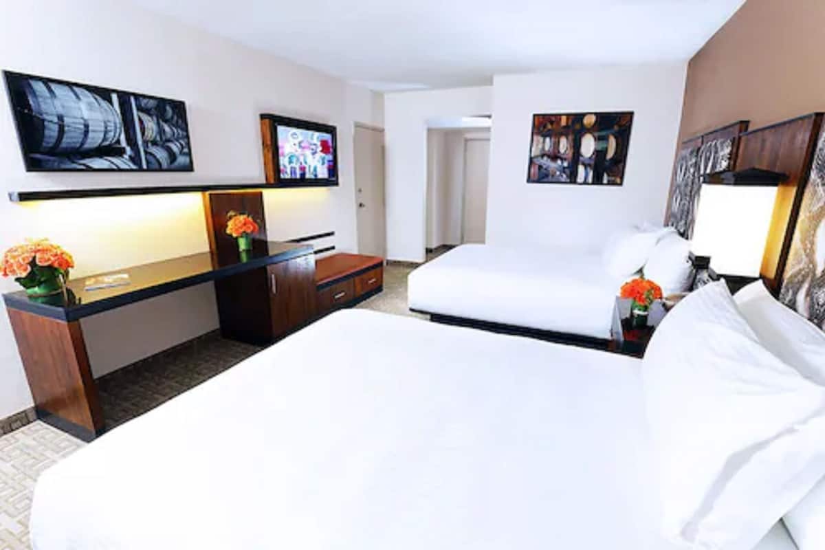 Ett hotellrum med två sängar, ett skrivbord, en stol, en TV och konstverk på väggarna.