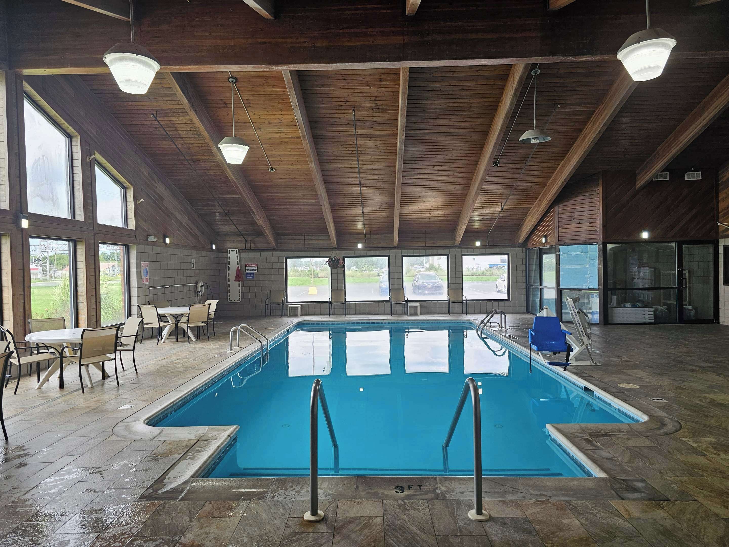 An indoor swimming pool with a wooden ceiling, large windows, and seating areas.