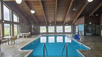 An indoor swimming pool with a wooden ceiling, large windows, and seating areas.