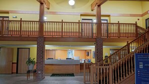 Un hall d’hôtel avec un escalier en bois, un comptoir d’accueil et un balcon situé au deuxième étage.