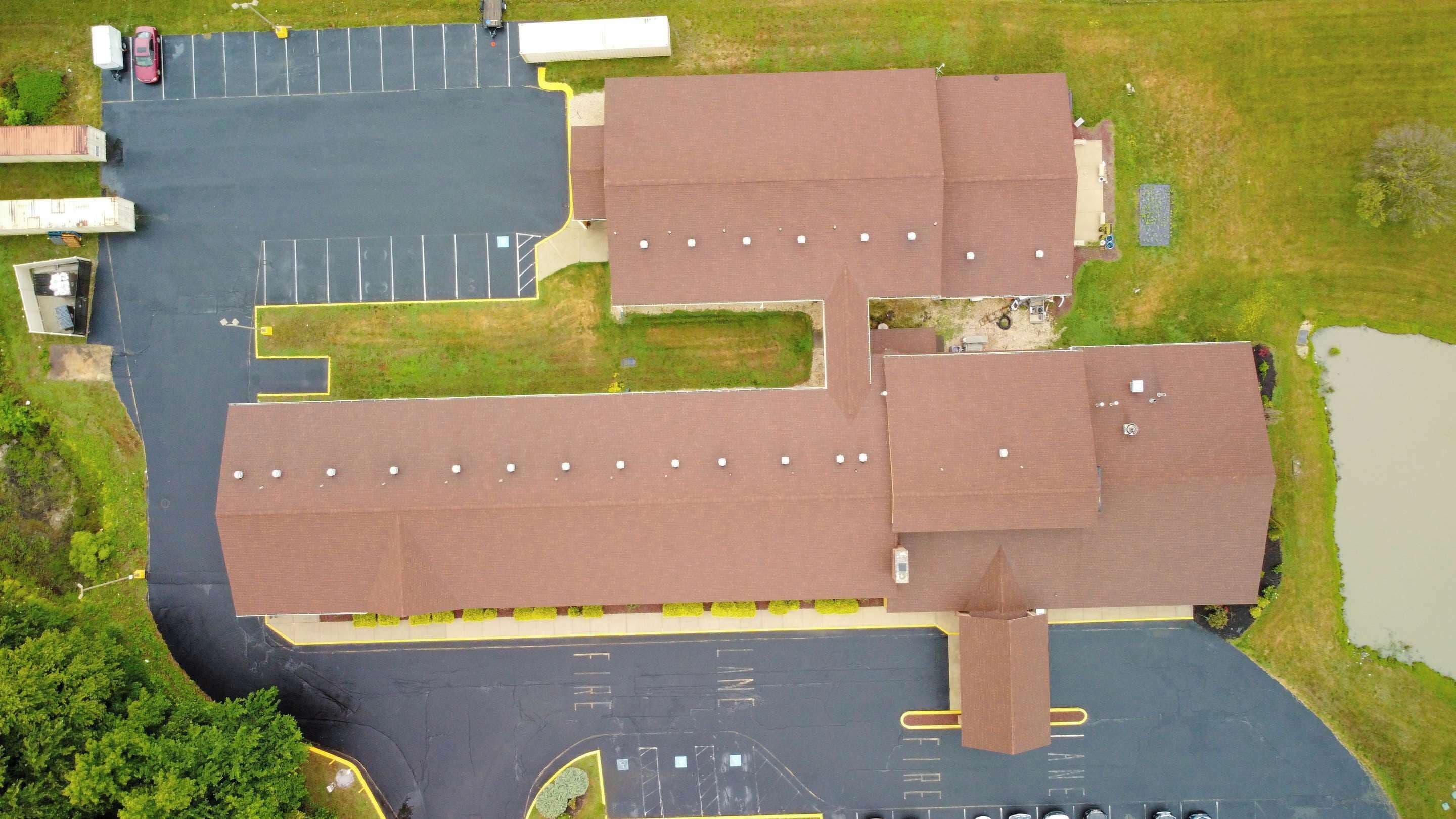 Vista aérea de un estacionamiento con múltiples espacios, un edificio de techo marrón y un pequeño estanque.