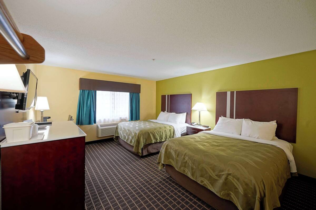 A hotel room with two beds, a desk, and a TV.