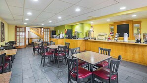 Un restaurant avec des tables et des chaises en bois, un comptoir où sont exposés des plats, et un escalier menant à un autre espace.