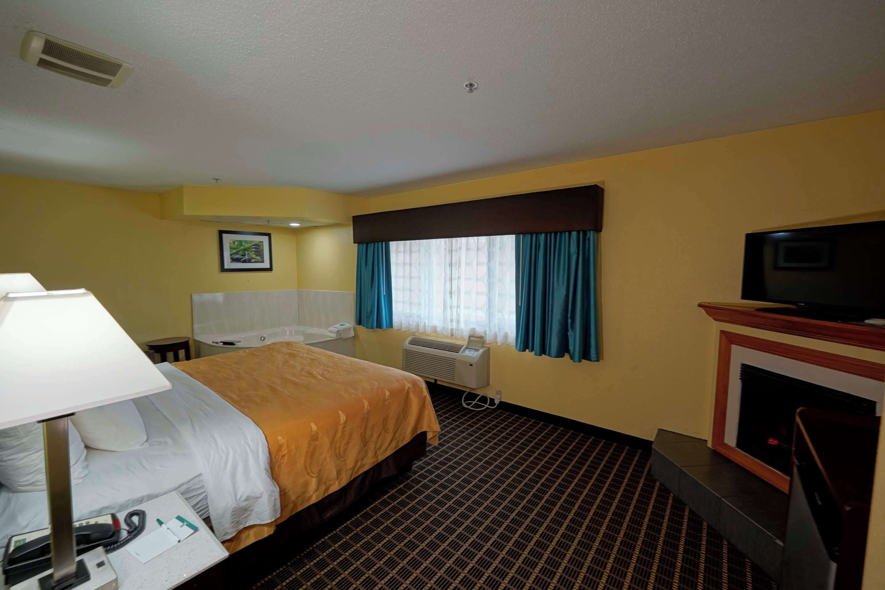 Habitación de hotel con cama, escritorio con lámpara, televisión, chimenea y ventana con cortinas.