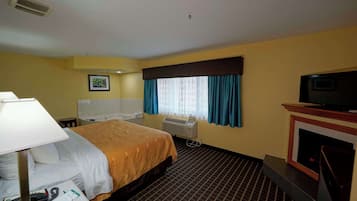 Habitación de hotel con cama, escritorio con lámpara, televisión, chimenea y ventana con cortinas.
