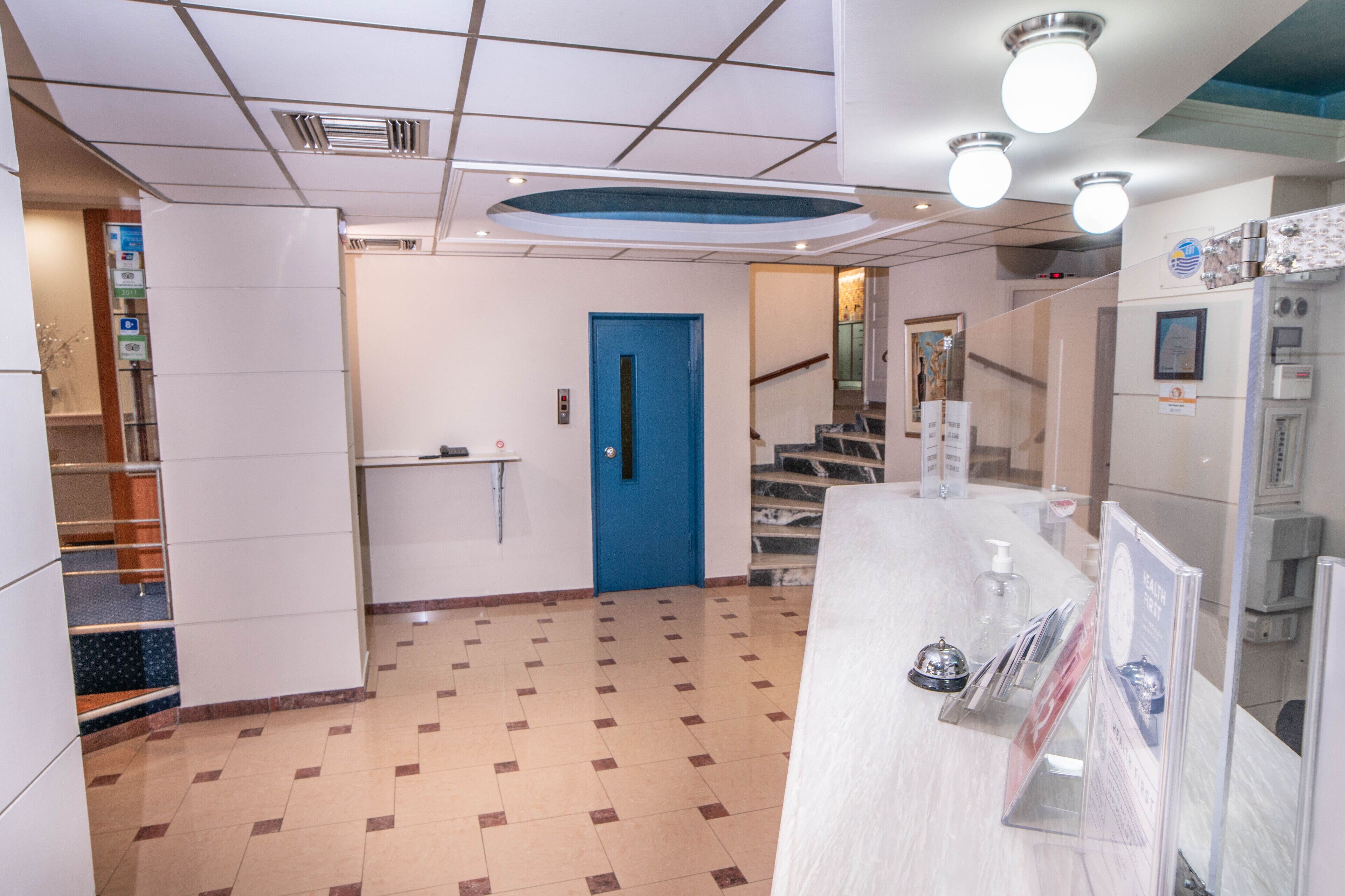 En hotellobby med en blå dörr, en receptionsdisk och en trappa som leder till ett annat våningsplan.