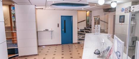 A hotel lobby with a blue door, a reception desk, and a staircase leading to another floor.