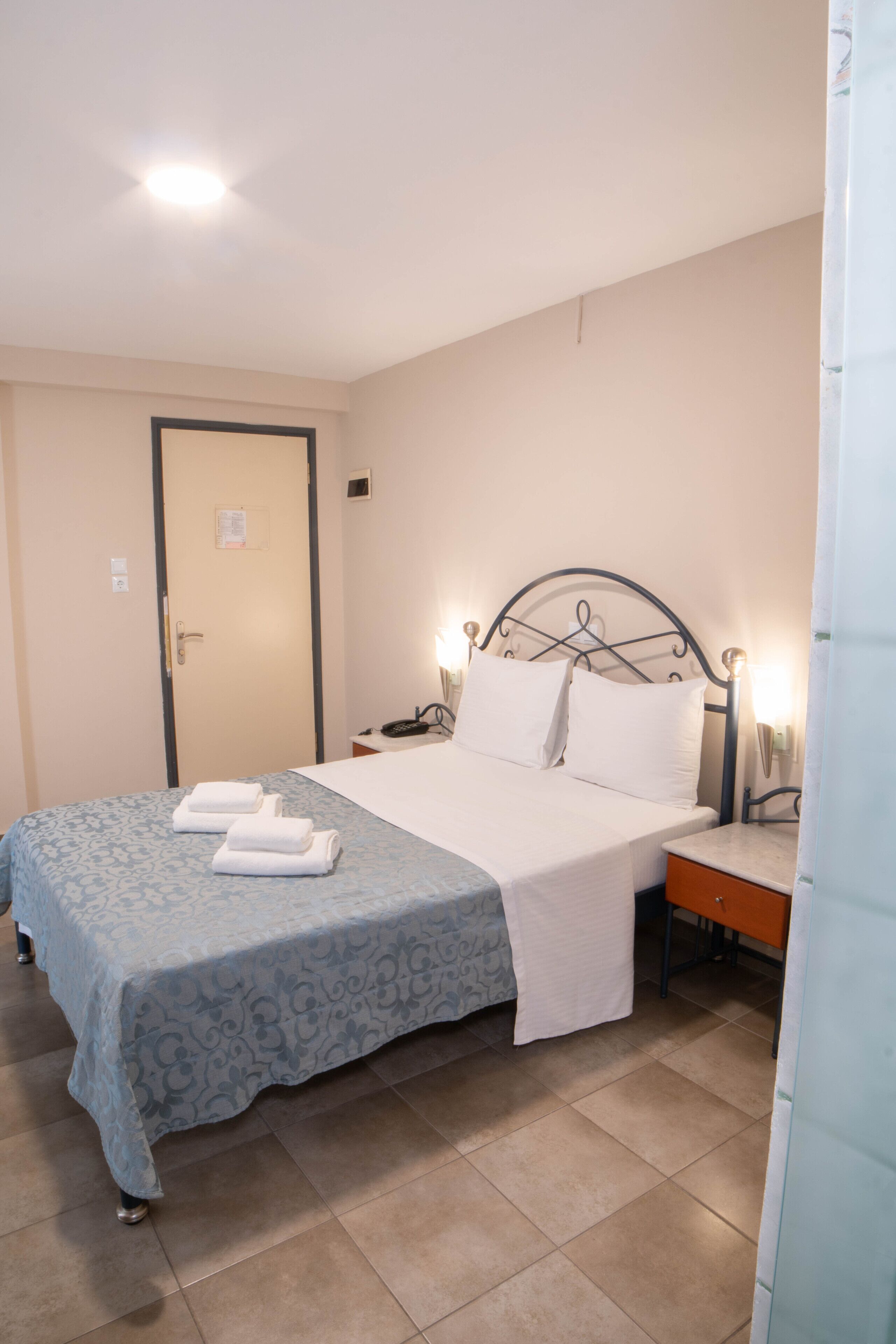 Una habitación de hotel con cama, mesita de noche y una puerta.