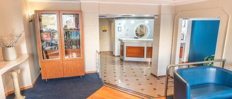 Un vestíbulo de hotel con un armario de madera, una silla azul y un mostrador de recepción.