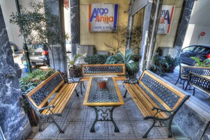 Un área de estar al aire libre con bancos de madera y una mesa, rodeada de plantas en macetas y un letrero que indica Hotel Argo Anita.