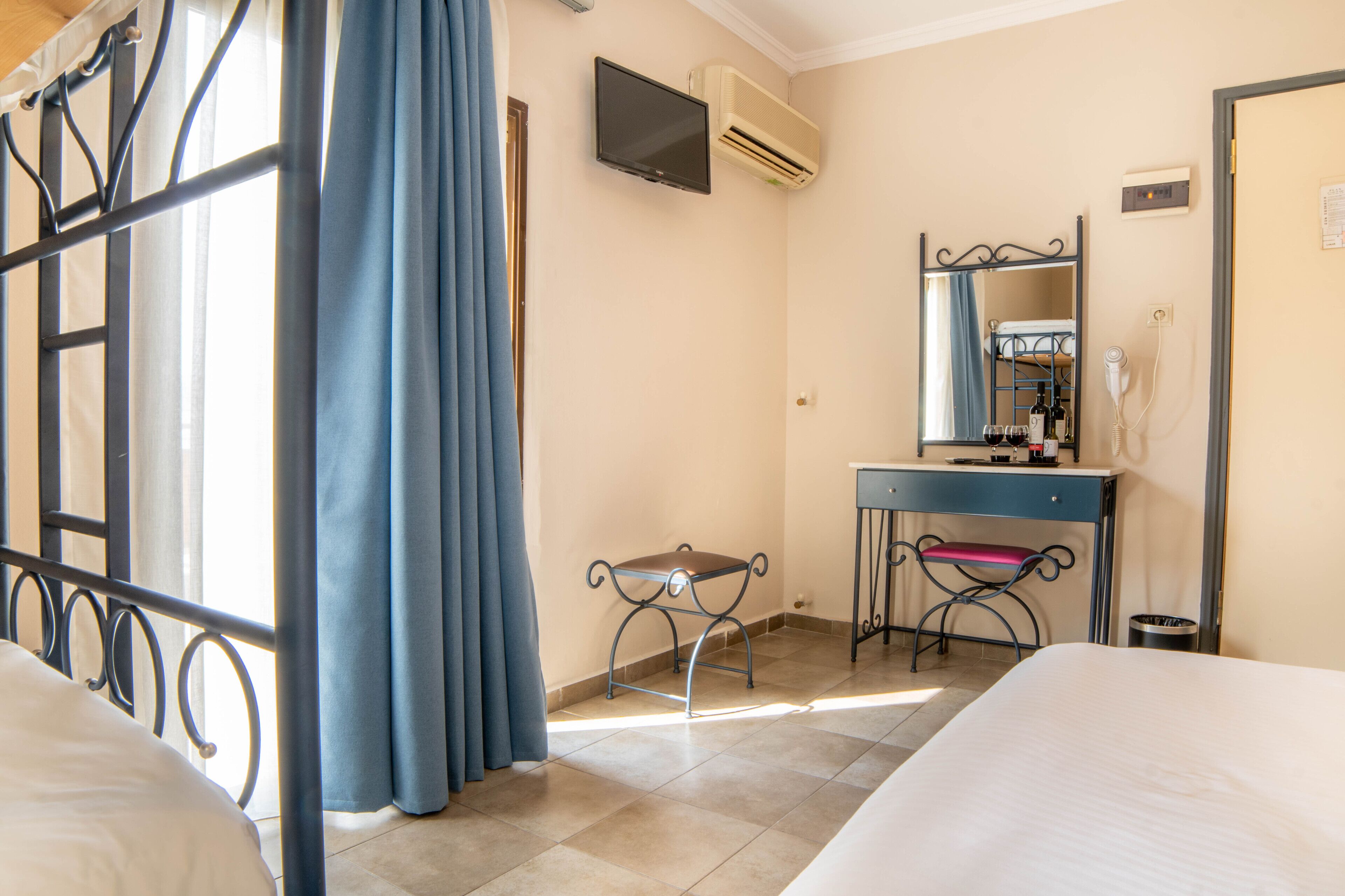 A hotel room with a bed, a desk with a chair, a TV, and an air conditioning unit.