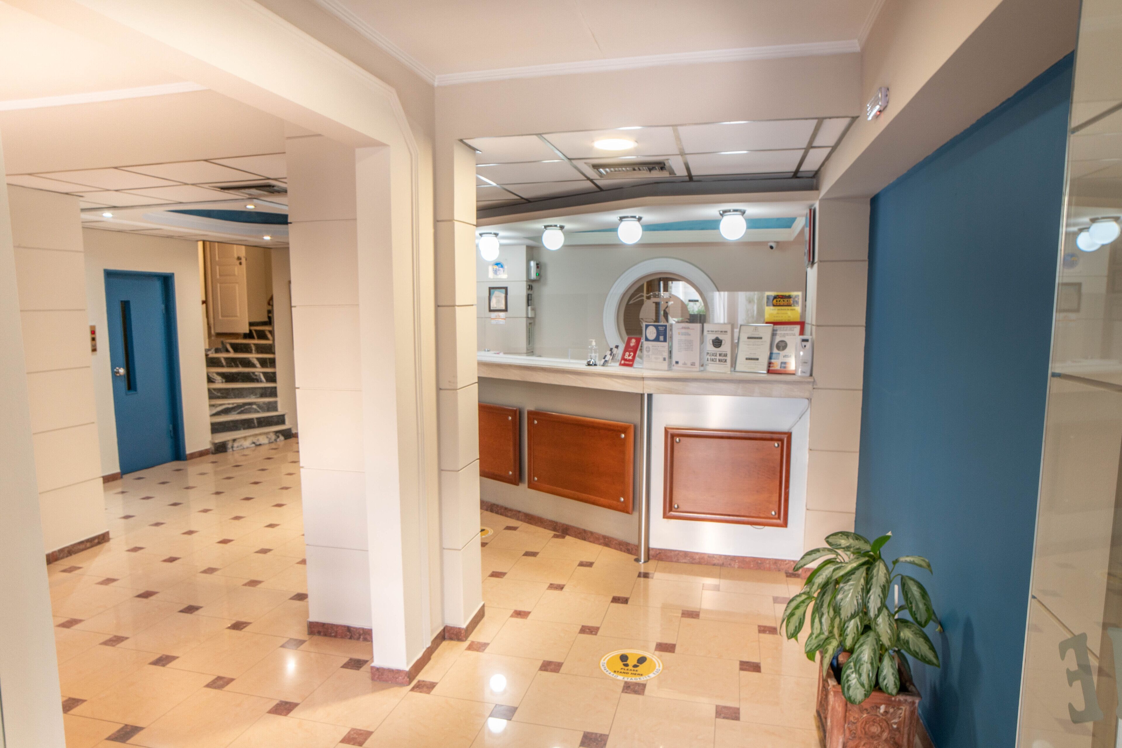 Un hall de hotel con mostrador de recepción, escalera y planta en maceta.