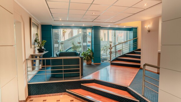 Un moderno vestíbulo de hotel con una escalera, zona de estar y plantas en macetas.