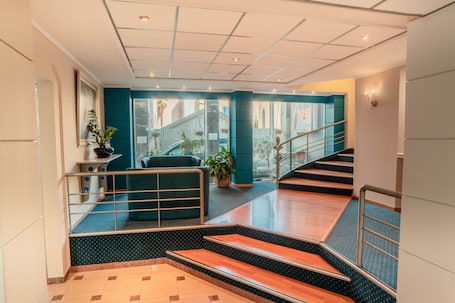 A modern hotel lobby with a staircase, seating area, and potted plants.