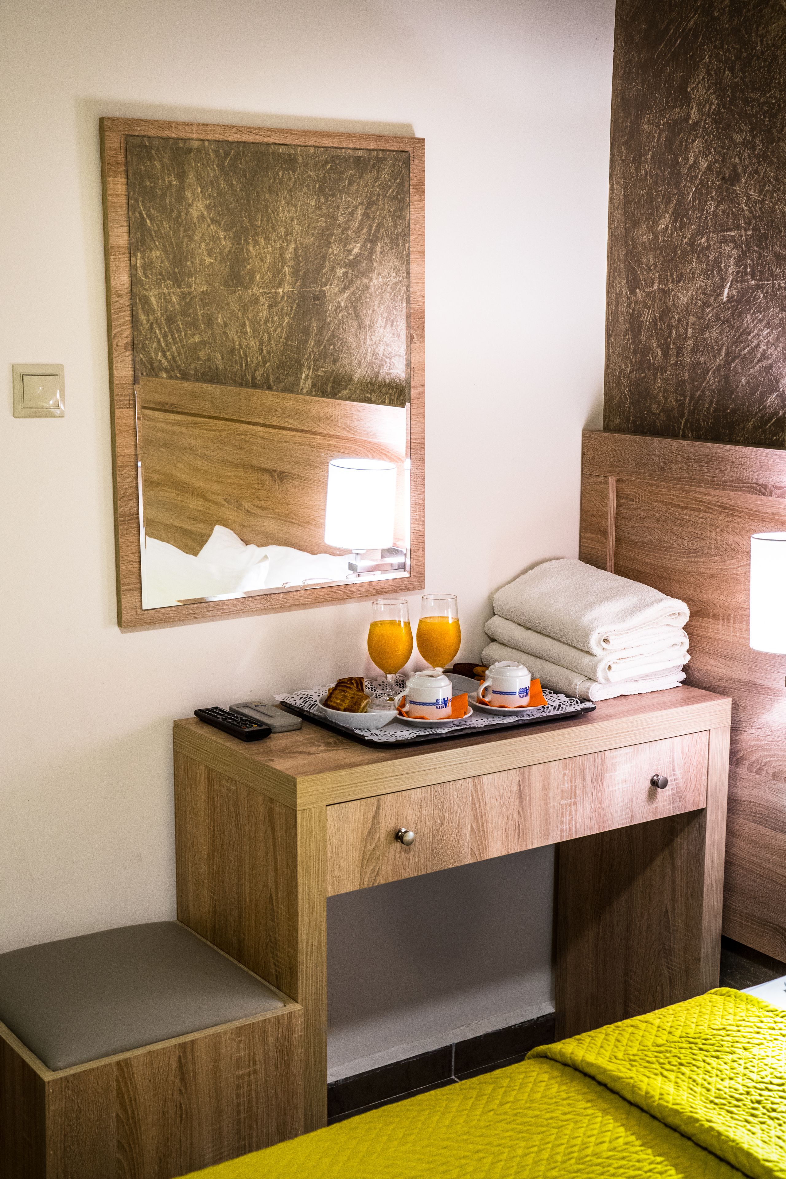 Un escritorio de madera con un espejo, una bandeja con jugo de naranja, una toalla y un control remoto.