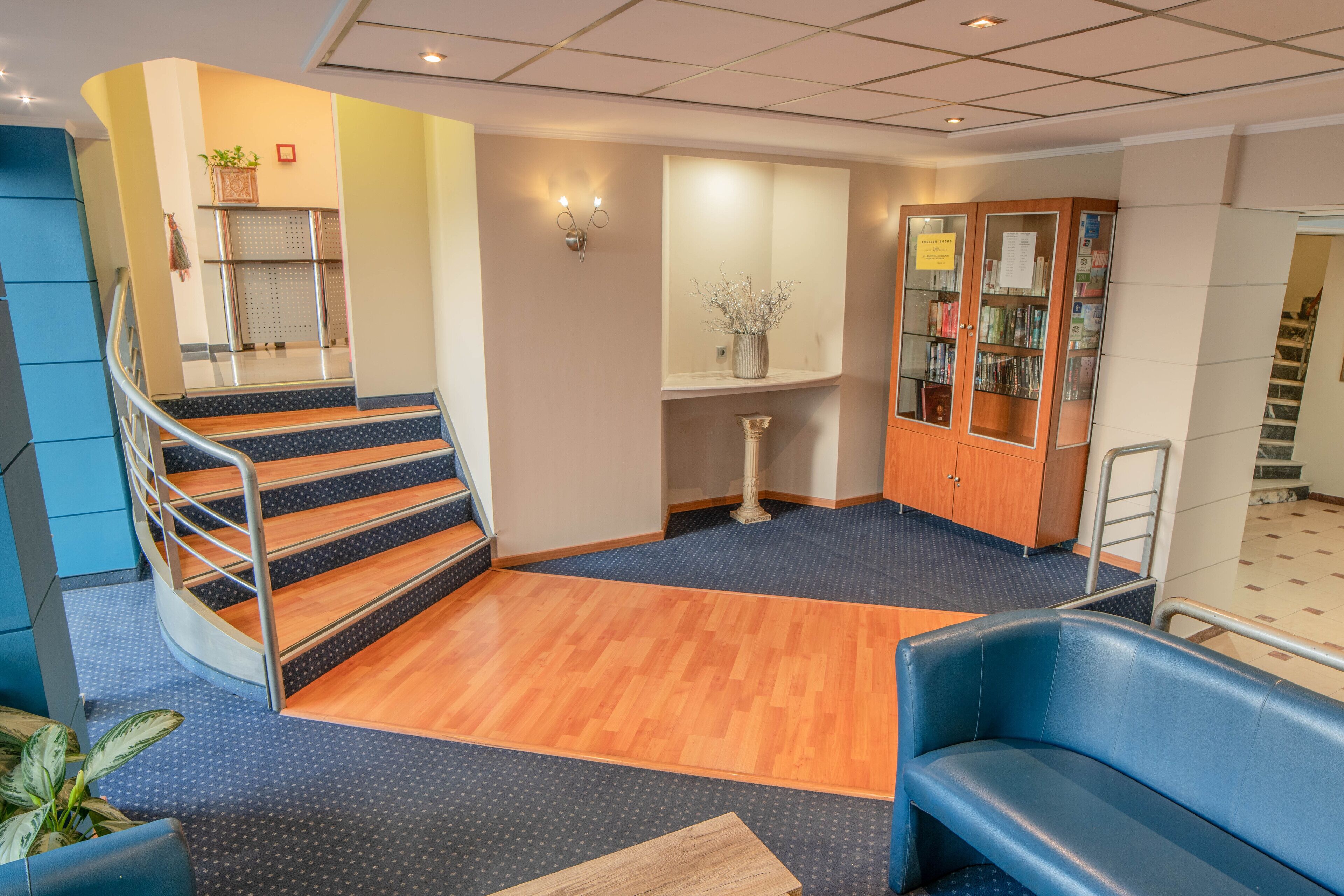 A lobby with a staircase, a reception desk, a seating area, and a bookshelf.