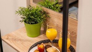 Una mesa de madera con un desayuno que incluye pasteles, una planta verde y dos vasos de zumo de naranja.
