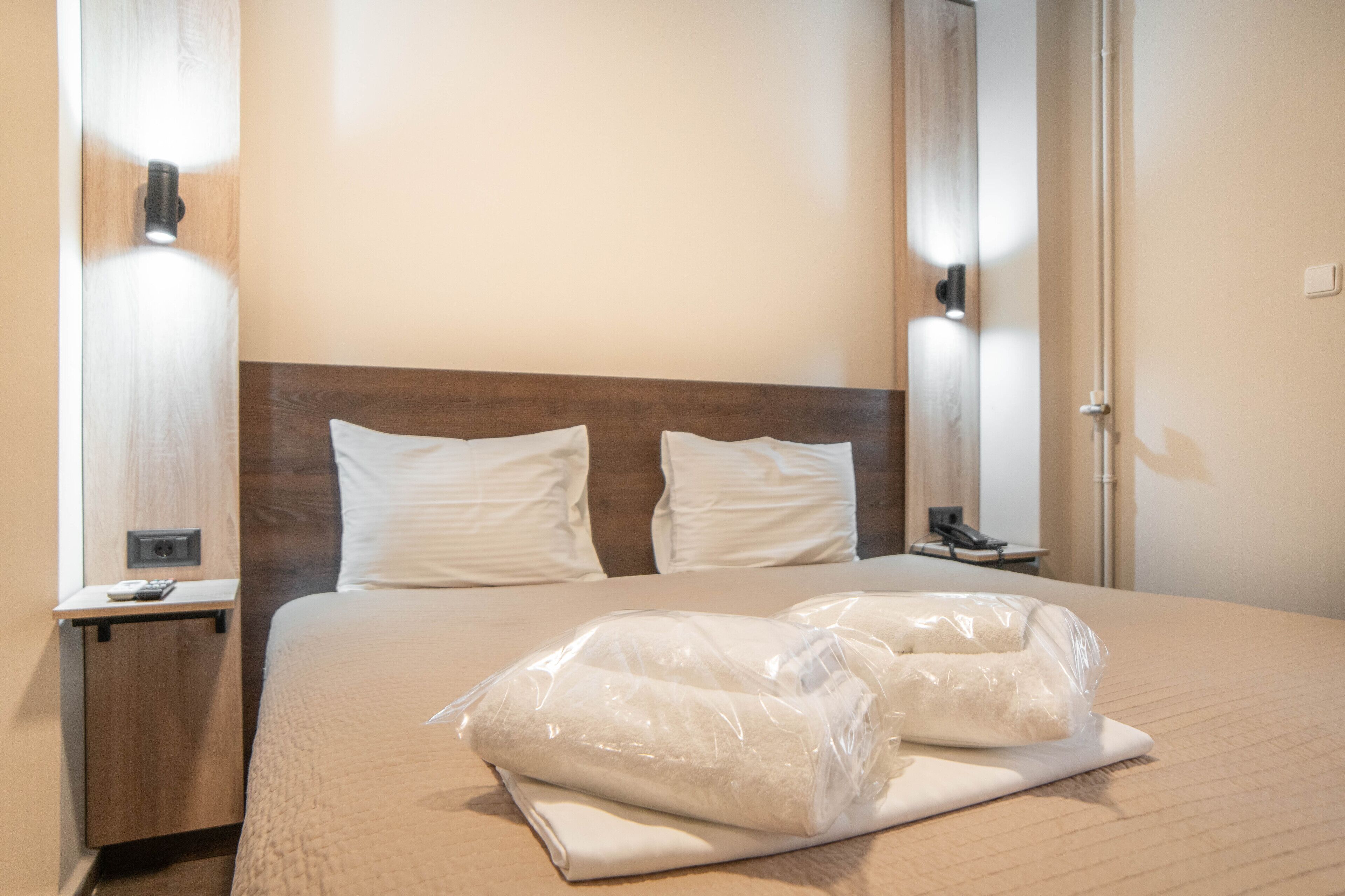 A hotel room with a neatly made bed, a wooden headboard, two bedside tables, and a wall-mounted light fixture.