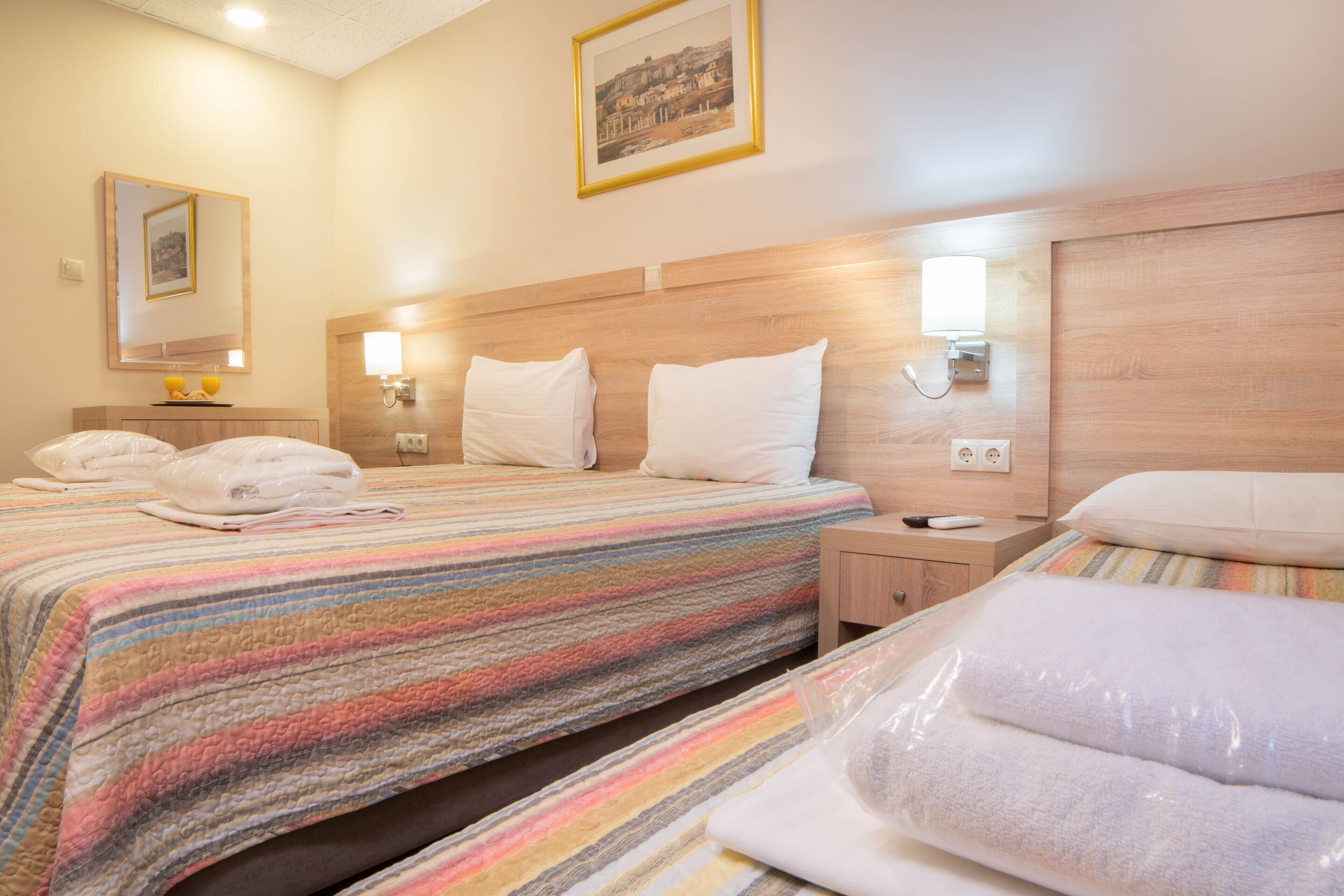 Een hotelkamer met een groot bed, een kleiner bed, een nachtkastje, een wandlamp en een lijst aan de muur.