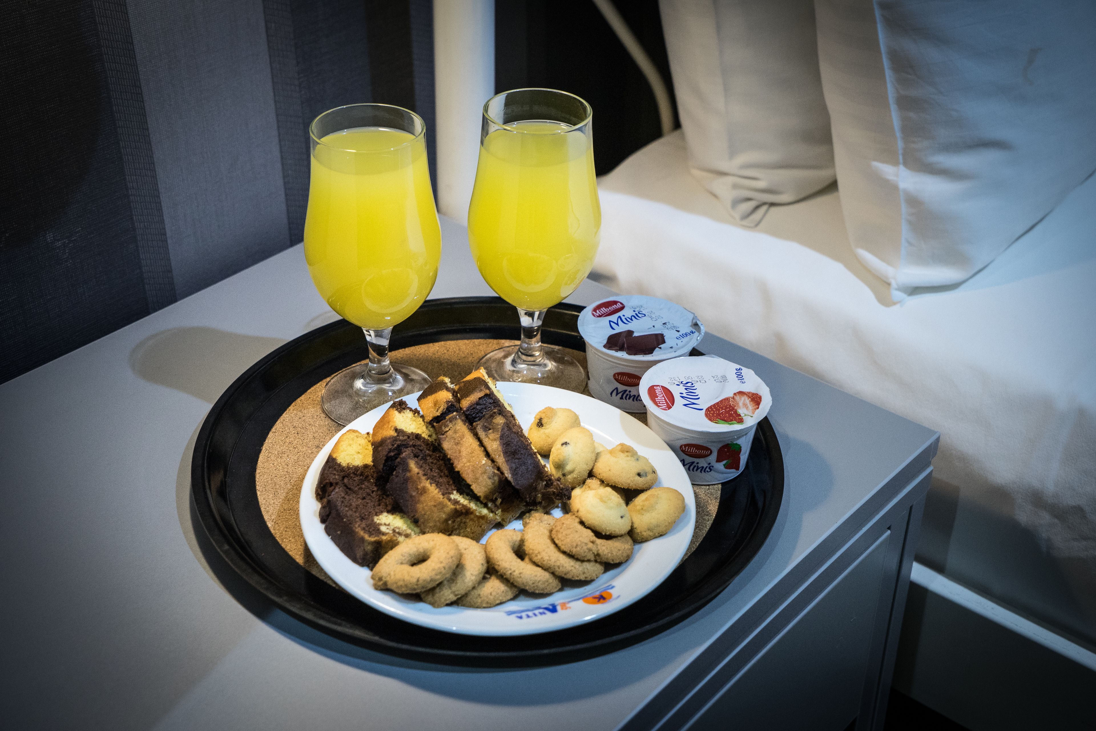 A tray with a plate of cookies, two glasses of orange juice, and two containers of yogurt on a hotel room table.