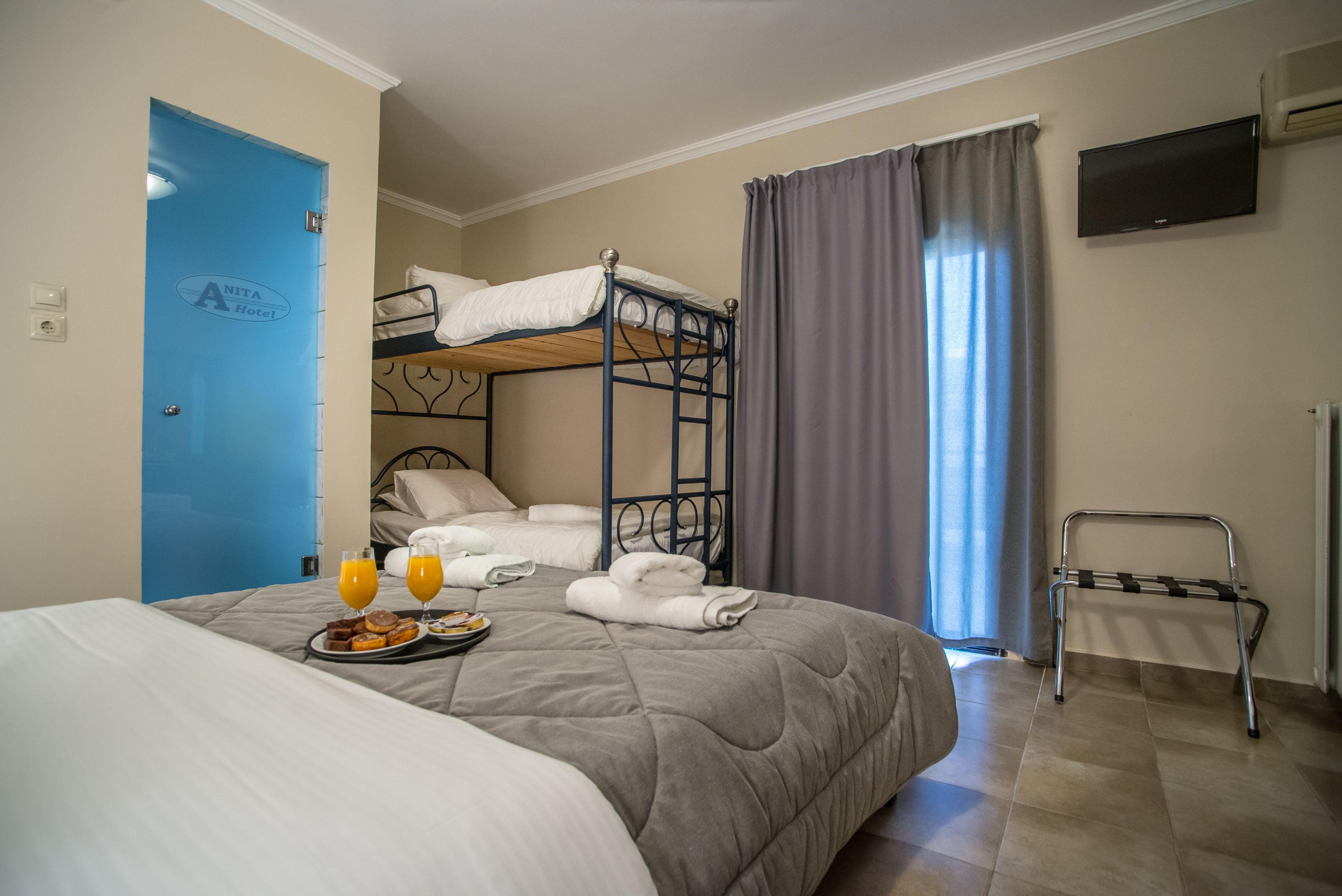 A hotel room with a bunk bed, a flat bed, a breakfast tray, and a TV on the wall.
