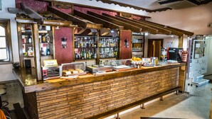 A bar area with a brick counter, shelves of bottles, a coffee machine, and a seating bench. - Argo Hotel (Piraeus)