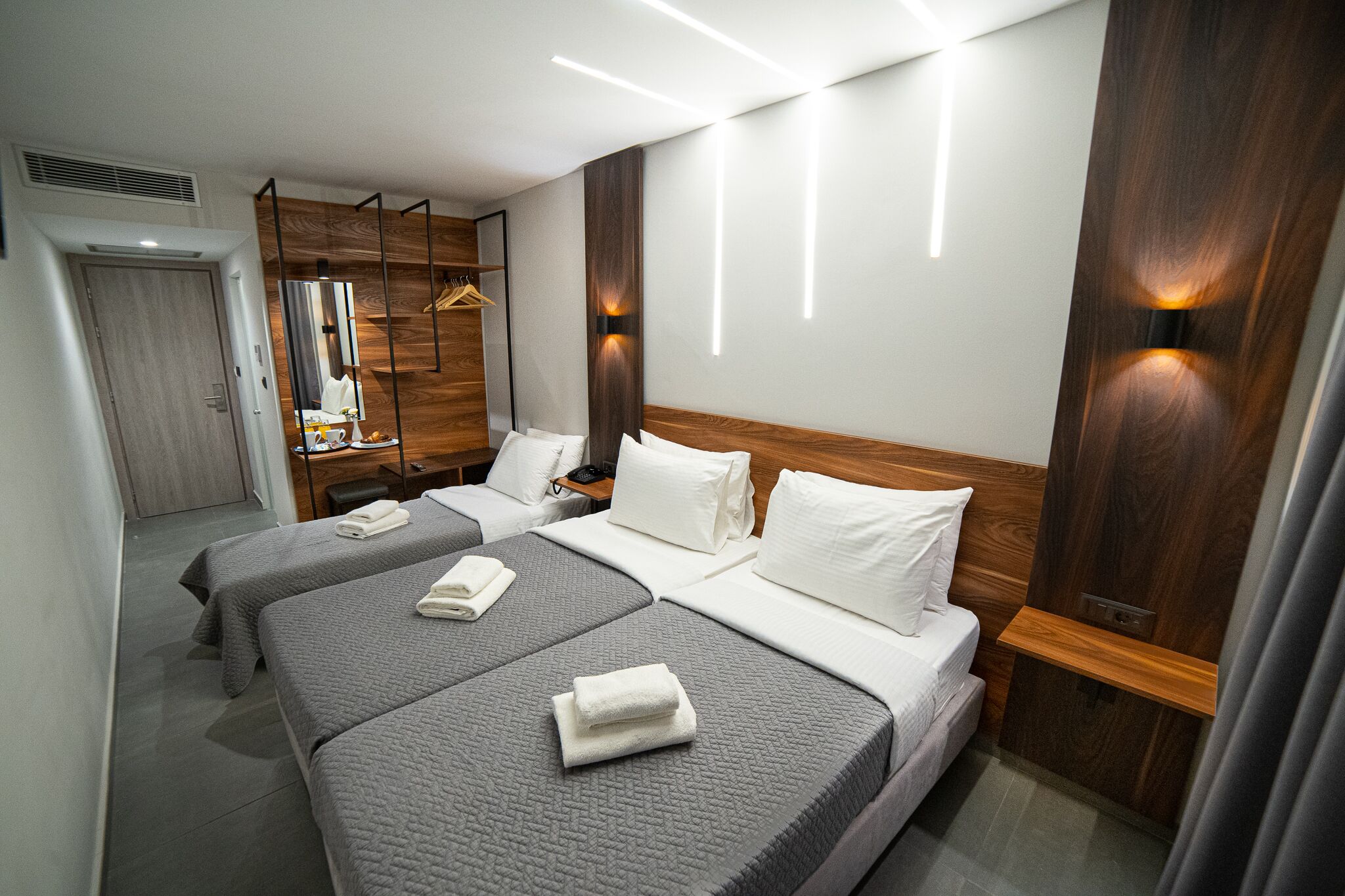 A hotel room with two beds, a mirror, a wardrobe, and a hanging coat rack.