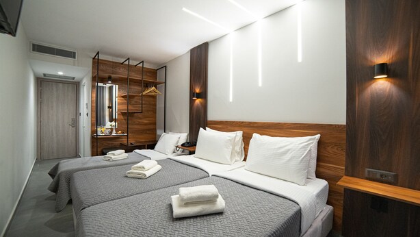 A modern hotel room with two beds, a wooden headboard, and built-in lighting. - Argo Hotel (Piraeus)