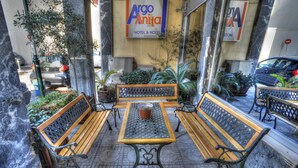 An outdoor seating area with wooden benches and a table, surrounded by potted plants and a sign for Argo Anita Hotel & Hotel. - Argo Hotel (Piraeus)