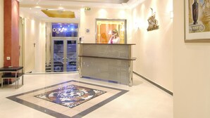 A hotel lobby with a reception desk, a patterned carpet, and a large mirror. - Argo Hotel (Piraeus)